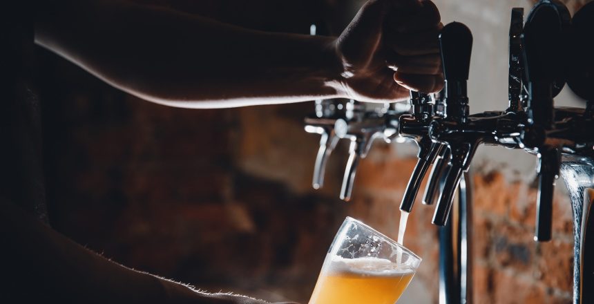 Light Draft cold beer pour in glass from crane in pub.