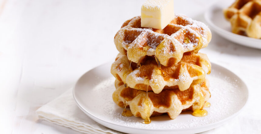 fresh baked waffles with syrup in a white plate on wooden background.